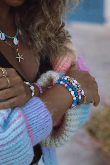 Bunte Armbänder und Kette, getragen von einer Person mit lockigen Haaren.